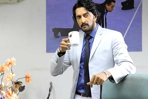 Kichcha Sudeep wearing a grey suit and holding a cup