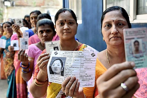 Women standing in line to vote, and holding up their Voter IDs