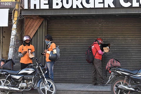 Two Swiggy delivery executives talk to each other while a Zomato delivery rider collects a food parcel