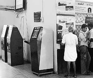 People standing in a queue to collect tickets at a counter in Egmore suburban station, while the automatic vending machines adjacent to the counter re