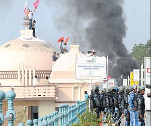 T activists climb atop the dome while security personnel stand guard on the Tank Bund in Hyderabad on Thursday. Also seen is smoke billowing out of a