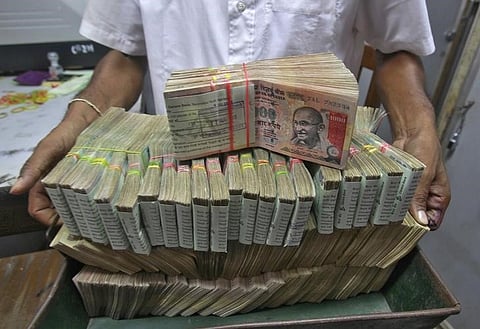 An employee poses with the bundles of Indian rupee notes inside a bank in Agartala |REUTERS