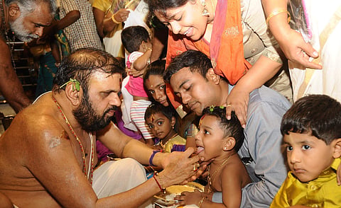 A priest initiates kids into the world of learning by writing on their tongues with golden rings, on the occasion of Vijayadasami. | EPS