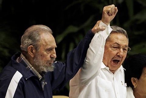 In this April 19, 2011 file photo, Fidel Castro, left, raises his brother's hand, Cuba's President Raul Castro, center, as they sing the anthem of international socialism. | AP