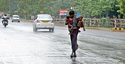 A man tries to cross a road with his children in the sudden downpour in Bhubaneshwar. 