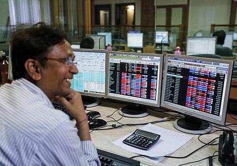 A broker laughs while speaking to a colleague, as they trade on their computer terminals at a stock brokerage firm in Mumbai. (Photo | Reuters)