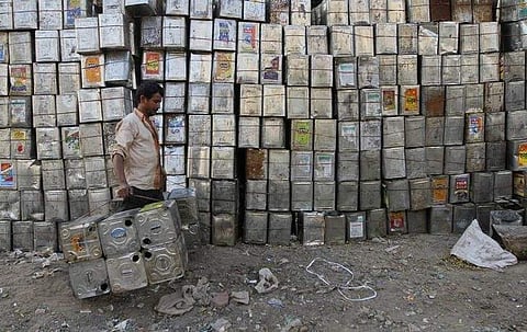 A man carries empty aluminium tins used for edible oil past a stack of tins at a recycling yard in Ahmedabad. (File Photo | Reuters)