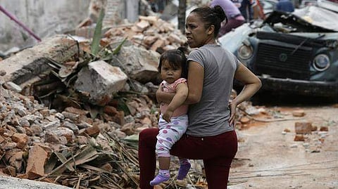 A woman holds her child as she stands next to wall turned to rubble when it collapsed during a massive earthquake, in Mexico City, Friday Sept. 8, 2017. | AP