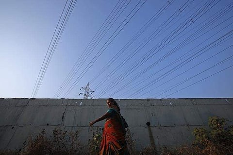 A woman walks under high-tension power lines leading from a Tata Power sub station in Mumbai's suburbs. (File Photo | Reuters)