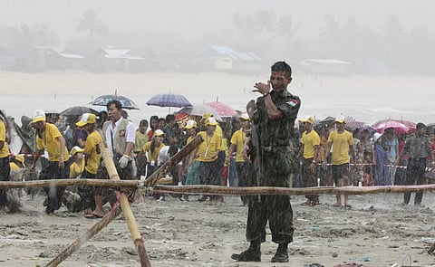 A soldier braves the monsoon rain as bodies recovered by fishing vessels in the waters off San Hlan village, in Laung Lone township, southern Myanmar, Thursday, June 8, 2017. (AP)