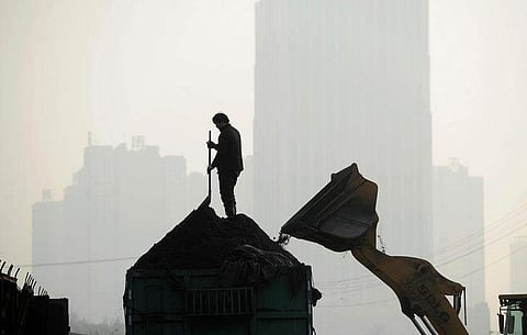 A worker stands on a truck as an excavator loads it with coal at a freight yard in Hefei, Anhui province. (File photo | Reuters)