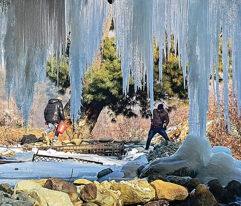 Men cross a stream as huge icicles hang from a bridge at Tangmarg in Baramulla,  Kashmir, on Sunday| PTI