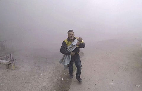 This photo provided by the Syrian Civil Defense group known as the White Helmets, shows what it says is one of its paramedics carrying his wounded son fleeing from the scene of an attack after airstrikes hit a rebel-held suburb near Damascus, Syria, Tuesday, Feb. 6, 2018. (AP)