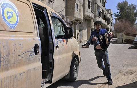 This photo released by the Syrian Civil Defense White Helmets, shows a member of the Syrian Civil Defense group carrying a boy who was wounded during airstrikes and shelling by Syrian government forces in Ghouta, a suburb of Damascus, Syria, Sunday, March