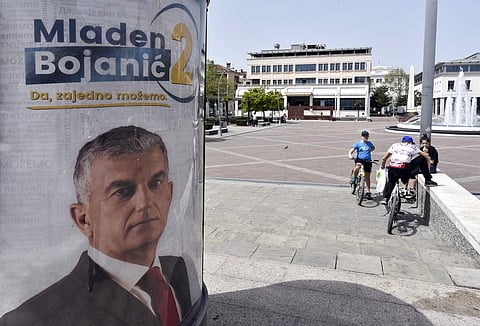 People rest near a billboard showing Mladen Bojanic, backed by a diverse group of parties, including a pro-Russian Democratic Front, reading: ''Mladen Bojanic - Yes, together we can'' in Montenegro's capital Podgorica.  (AP)
