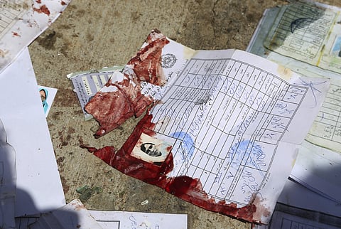 Blood-stained national ID papers of a woman and voters' photos are seen on the ground outside a voter registration center, after a suicide attack in Kabul, Afghanistan, Sunday, April 22, 2018. Gen. Daud Amin, the Kabul police chief, said the suicide bombe