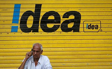 A man speaks on his mobile phone as he sits in front of a shop displaying the Idea Cellular Ltd's logo on its shutter in Mumbai. | Reuters