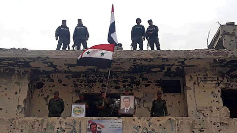 In this photo released by the Syrian official news agency SANA, Syrian military and police forces fly their national flags on a damaged building and hold a picture of Syrian President Bashar Assad, in the Hajar al-Aswad neighborhood, southern Damascus, Sy
