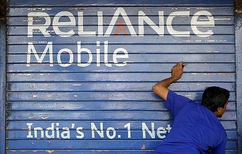 A man opens the shutter of a shop painted with an advertisement of Reliance Communications in Mumbai. File photo | Reuters