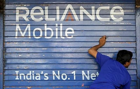 A man opens the shutter of a shop painted with an advertisement of Reliance Communications in Mumbai, India, November 3, 2015. | Reuters