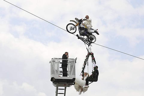 Pastor Stefan Gierung, left, stands in a cage atop of a fire service ladder in front of bride Nicole Backhaus, center, and groom Jens Knorr, right, both sitting in a swing dangling under a motorcycle with artist Falko Traber, top, during the wedding cerem