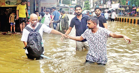 People walk along a flooded street during heavy showers in Mumbai. (File  | EPS/Bhushan Loyande)