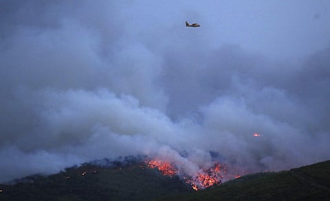 Gale-fanned wildfires raged through holiday resorts near Greece's capital, killing at least 20 people by early Tuesday and injuring more than 104, including 11 in serious condition. A plane flies over the smoke and fire coming the town of Mati, east of At