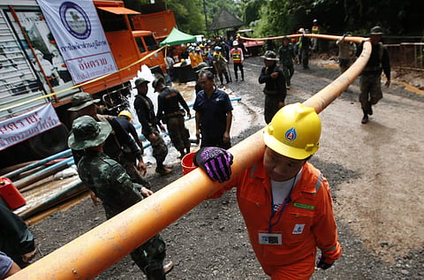 Rescuer carrying water pipe makes their way up at the entrance to a cave complex where 12 boys and their soccer coach were trapped inside when heavy rains flooded the cave, in Mae Sai, Chiang Rai province, in northern Thailand, Wednesday, July 4, 2018. | 