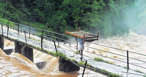 A flood-affected man carries the last of his belongings across the overflowing Deviyar river in Valara near Adimaly on Thursday.  | (A Sanesh | EPS)
