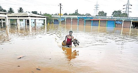 A man carrying an LPG cylinder and a stove wades through the flooded Kushalnagar-Hassan Road in Kodagu on Thursday | Udayshankara S