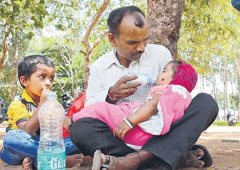 A man waits with his children outside a VRO exam center as his wife attends the exam, in Sangareddy on Sunday |  Express
