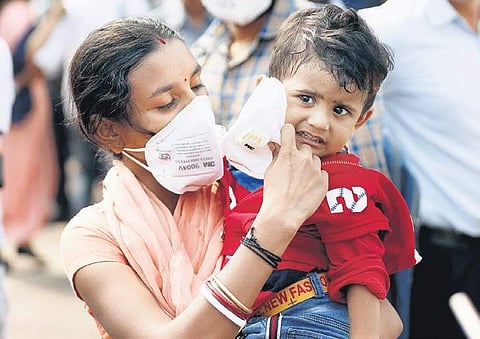 A woman puts an anti-pollution mask on a child’s face, in New Delhi. | ( Photo | Arun Kumar )