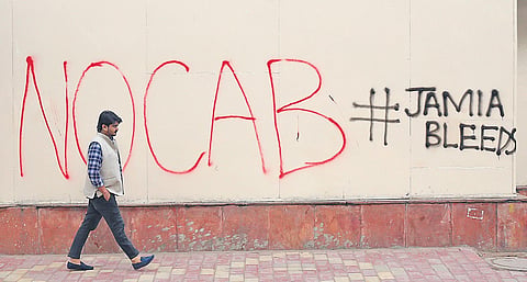 A man passes by a wall with graffiti about the recently amended Citizenship Act, outside Jamia Millia Islamia | arun kumar