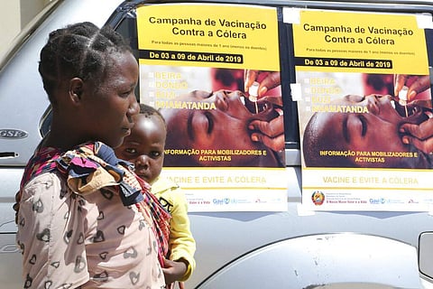A woman and her baby walk past cholera vaccination campaign posters on the first day of the cholera vaccination programme at a camp for displaced survivors of cyclone Idai in Beira, Mozambique. (Photo | AP)