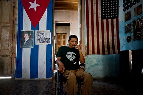 A man poses next to Cuban and US flags at his home, with the Cuban one carrying photos of Fidel and Raul Castro, in Havana, Cuba (File Photo  | AP)