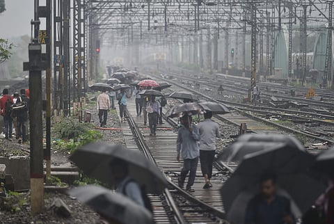 People walk on the railway tracks as heavy monsoon rains hit the central suburban trains service in Mumbai on 2 July 2019. (Photo | PTI)
