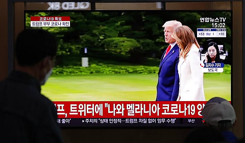 People wearing face masks watch a TV screen reporting about U.S. President Donald Trump and first lady Melania Trump at the Seoul Railway Station, South Korea. (Photo | AP)