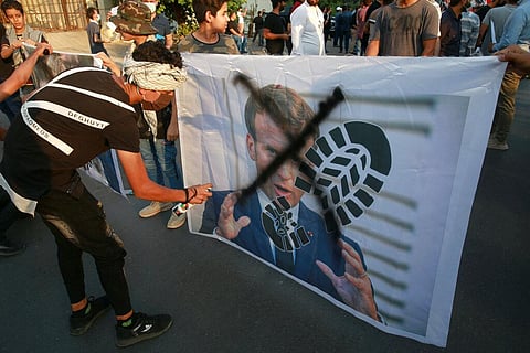 Protesters deface a picture of French President during a protest over caricatures of the Prophet Muhammad they deem insulting and blasphemous, outside the French Embassy, in Baghdad. (Photo | AP)