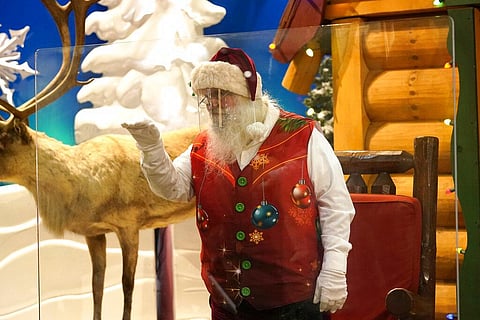 Santa Claus waves at children and their families from behind a transparent barrier at a shop in Miami.  (Photo | AP)
