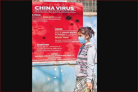 A woman wearing a mask walks past an awareness board on Novel Coronavirus at a Kolkata hospital. (Photo | PTI)