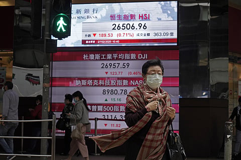 A woman walks past an electronic board showing Hong Kong share index outside a local bank in Hong Kong, Thursday, Feb. 27, 2020. Shares fell in Asia on Thursday after President Donald Trump announced the U.S. was stepping up its efforts to combat the viru