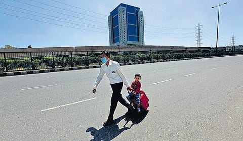 A migrant labourer makes the journey back to his village on foot with his son on the Delhi-Jaipur national highway near Gurugram on Saturday | SHEKHAR YADAV