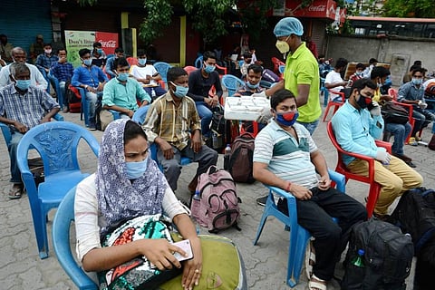 A volunteer distributes food among the passengers waiting to board a bus for their hometown during ongoing COVID-19 lockdown in Guwahati on Tuesday. (Photo | PTI)