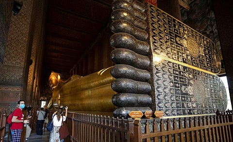 In this Friday, March 13, 2020, photo, tourists take a photograph with the statue of a giant Buddha at Wat Pho in Bangkok, Thailand. Wat Pho, which is one of Thailand's major tourist attractions and famous for housing the golden 46-meter-long (151-foot-lo