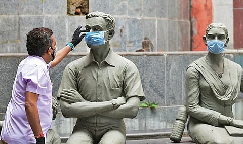 A man fixes masks onto statues at KSR Railway Station in Bengaluru, to build awareness on coronavirus, on Wednesday morning I Meghana Sastry