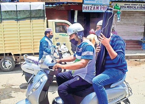 Two men carry an oxygen cyclinder on a two-wheeler while riding through Padarayanapura in Bengaluru on Wednesday | pandarinath b