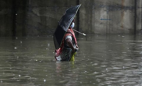 A woman wearing a mask as a precaution against the coronavirus walks through a waterlogged street during monsoon rains in Mumbai. (Photo | AP)