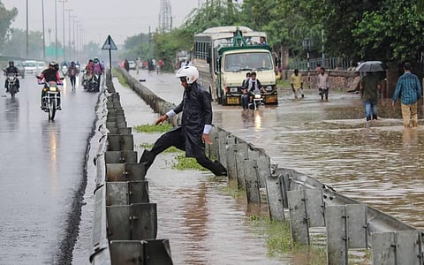 A man crosses a waterlogged divider at Delhi-Gurugram Expressway after heavy rains at Narsinghpur in Gurugram Thursday Aug 13 2020. (Photo | PTI)