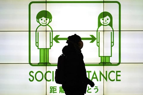 A woman wearing a protective mask to help curb the spread of the coronavirus walks in front of social distancing notice. (Photo | AP)