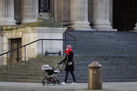 A woman wearing a face mask to curb the spread of coronavirus pushes a child in a buggy past the steps of St. Paul's Cathedral, in the City of London financial district of London. (Photo | AP)